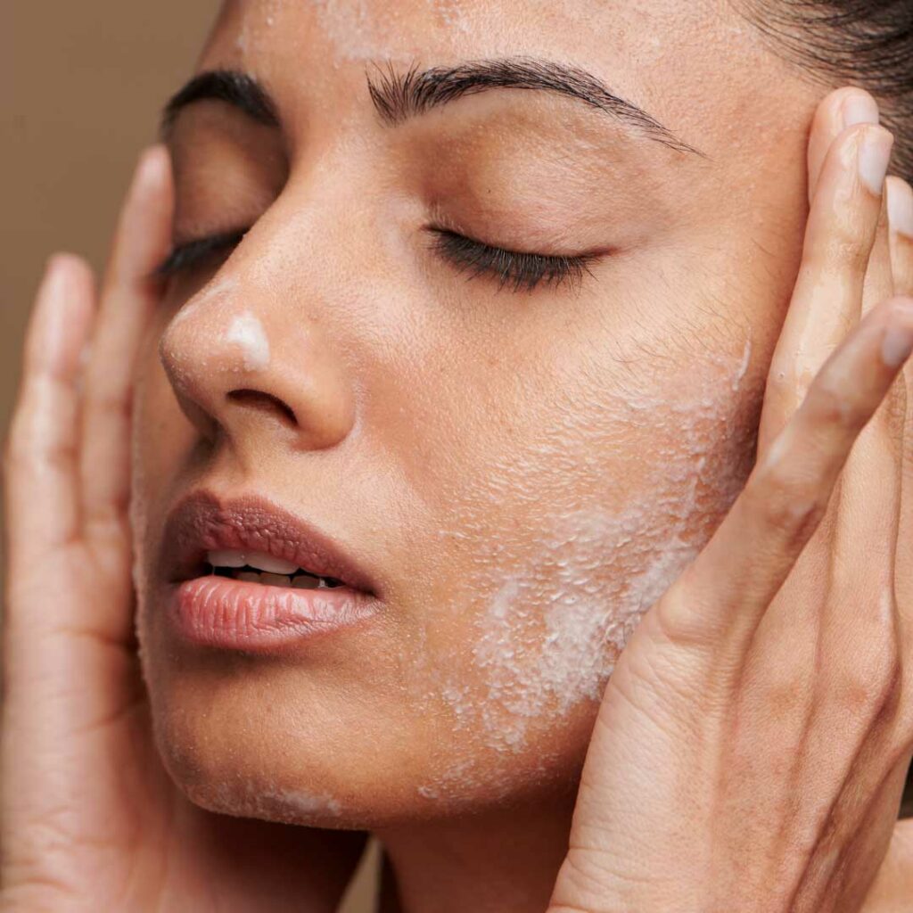 A woman with clean, radiant skin gently washing her face with a peptide-infused skincare product